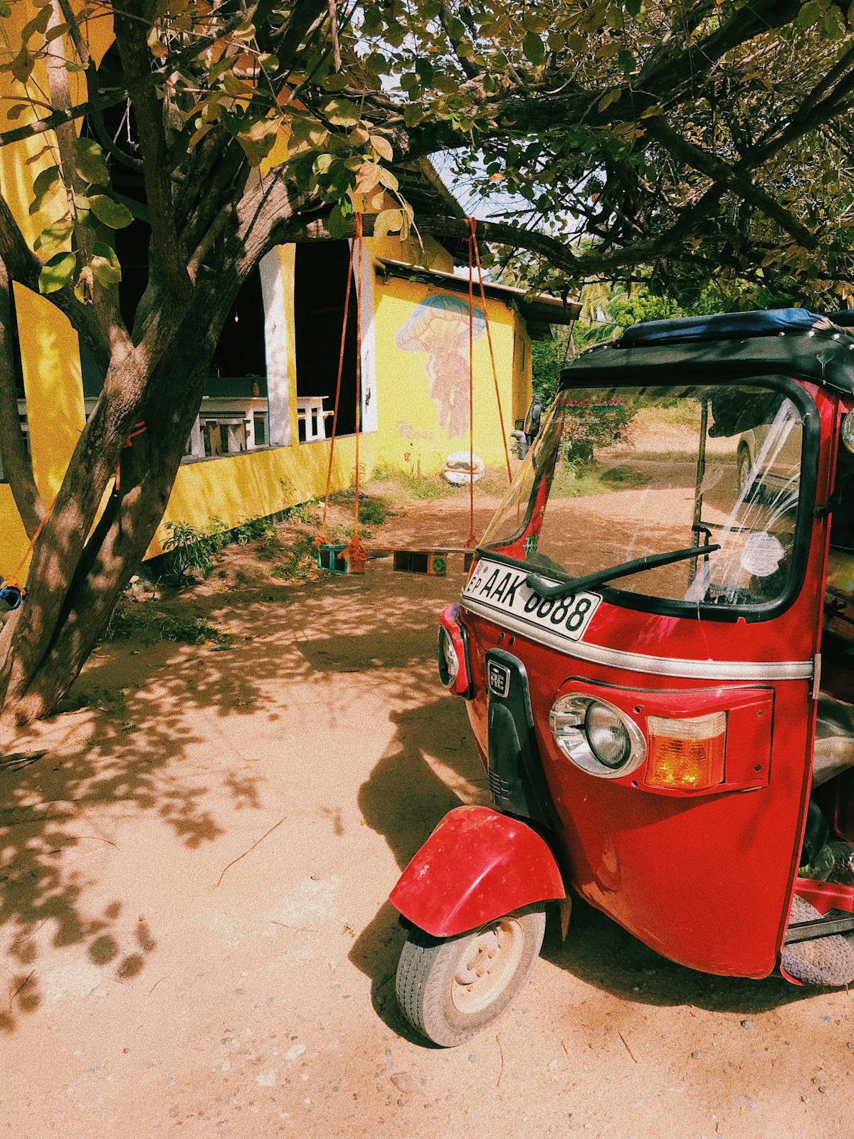 A red tuk-tuk parked under trees in a quiet Arugam Bay village street - the kind of unhurried scene that defines the east coast experience