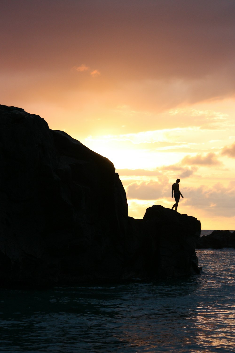 silhouette of person standing on rock formation during sunset