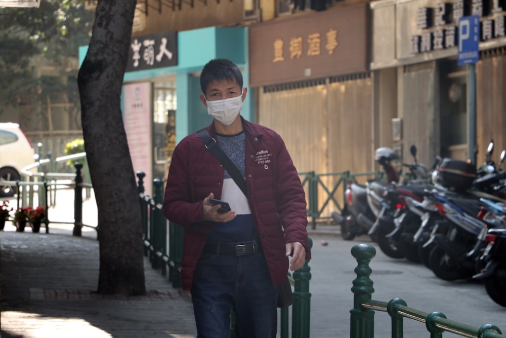 man in red jacket standing beside green metal fence during daytime