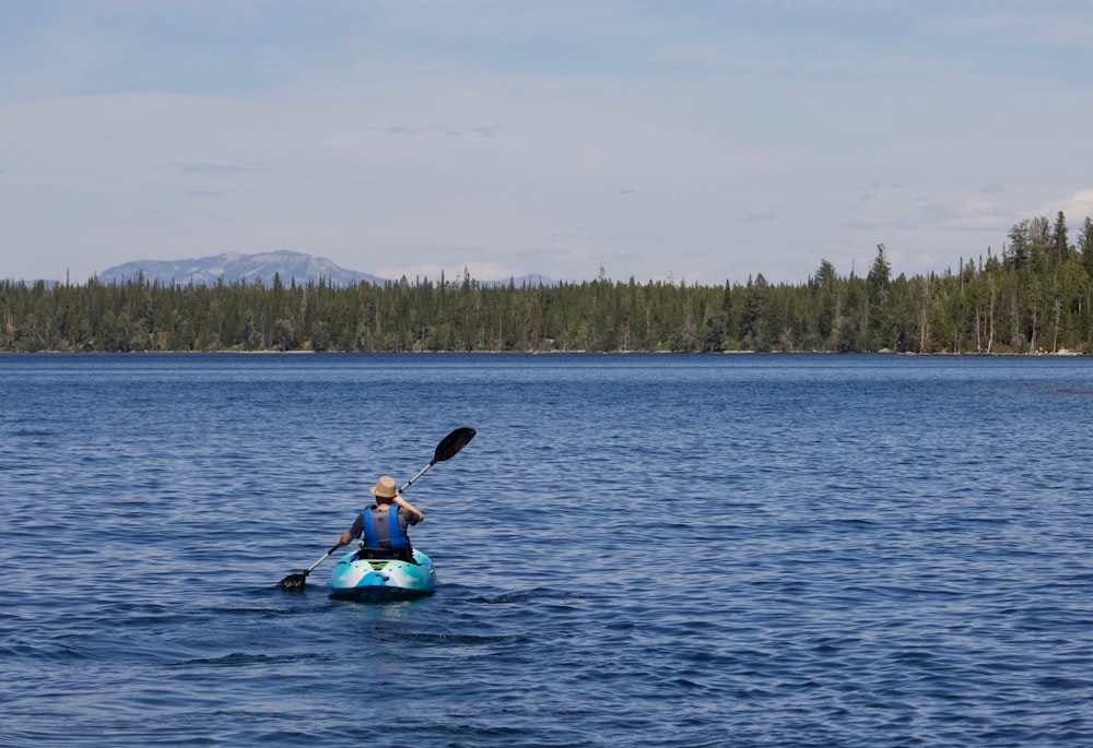 woman in blue and black wetsuit riding on blue kayak on blue sea during daytime