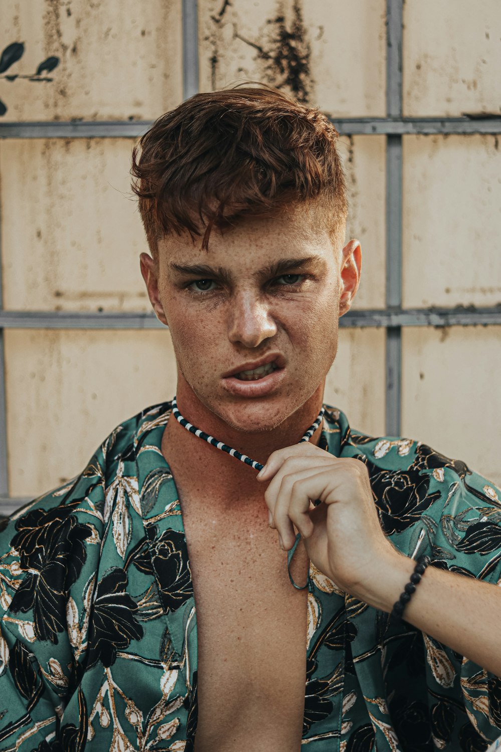 man in green and white floral shirt wearing blue beaded necklace