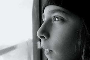 A close-up of a person gazing thoughtfully out a window.