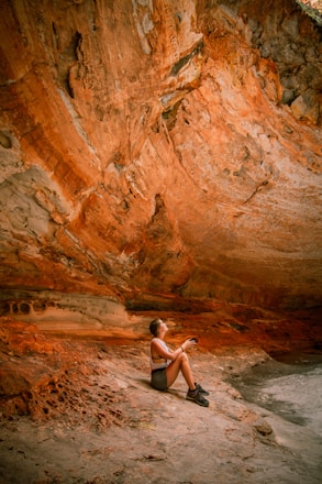 woman in white tank top sitting on rock formation during daytime