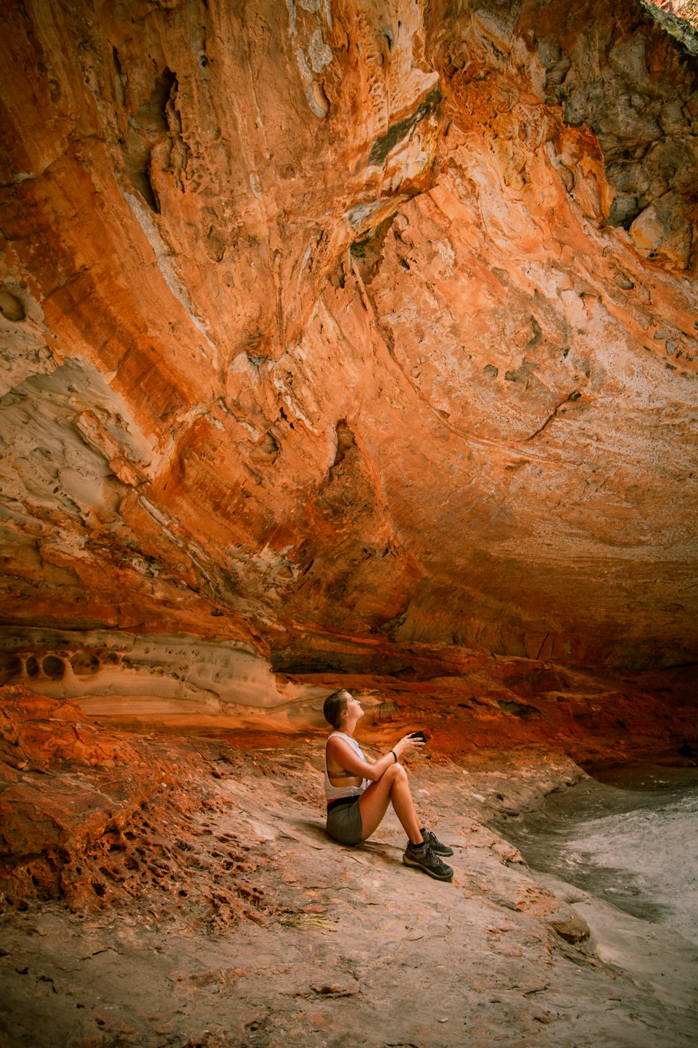 woman in white tank top sitting on rock formation during daytime
