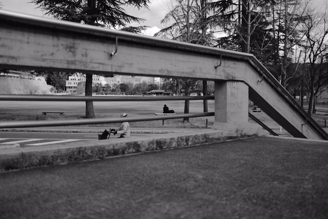 grayscale photo of man sitting on bench near trees