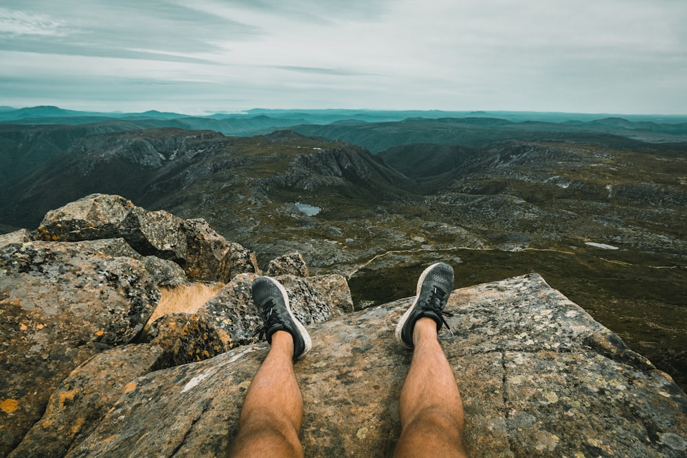 person in black and white sneakers sitting on rock