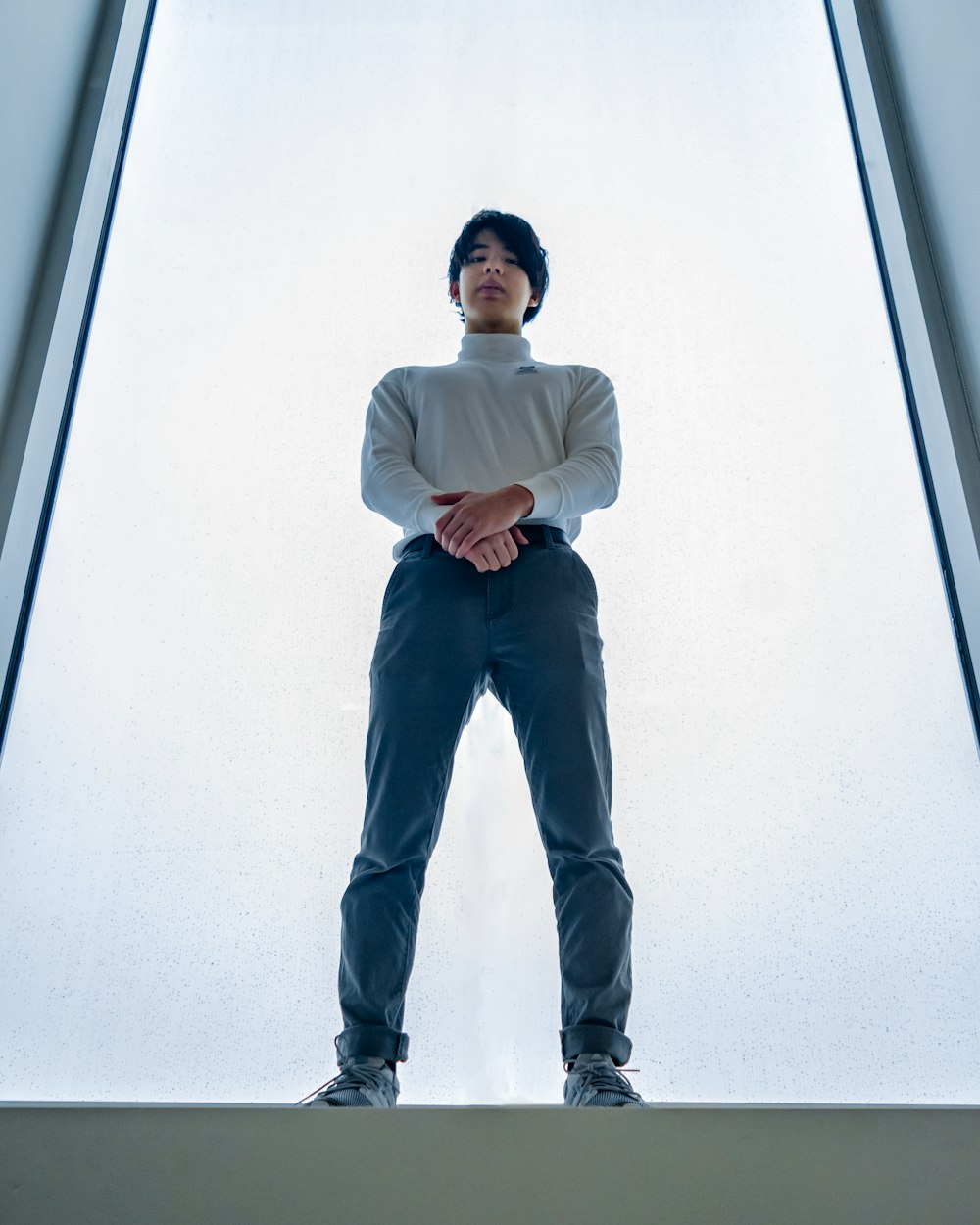 man in white dress shirt and black pants leaning on white wall