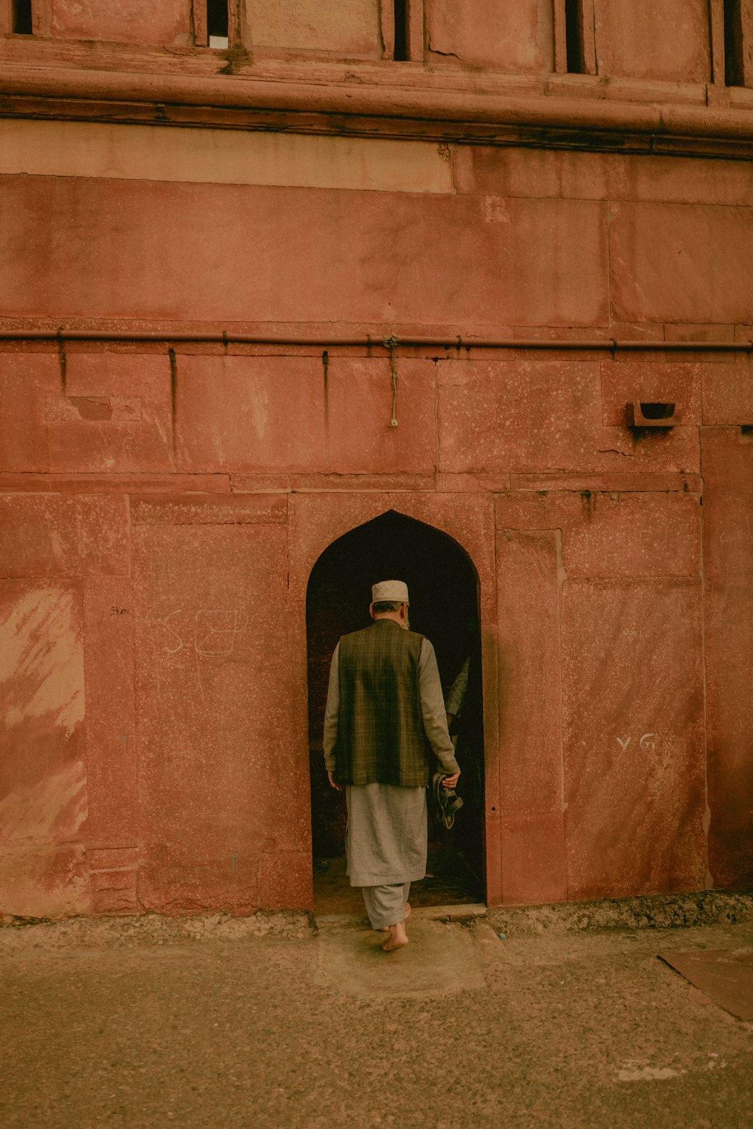 man in green and white robe standing in front of brown concrete wall