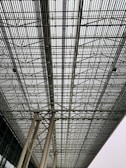 A large intricate metal grid structure supported by tall columns. The perspective of the image emphasizes the repetitive pattern and industrial design, creating a sense of depth and complexity.