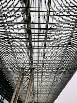 A large intricate metal grid structure supported by tall columns. The perspective of the image emphasizes the repetitive pattern and industrial design, creating a sense of depth and complexity.