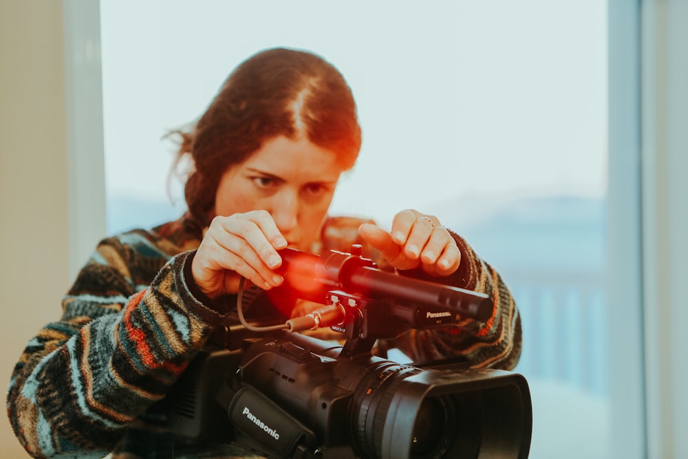 man in black and brown sweater holding red dslr camera