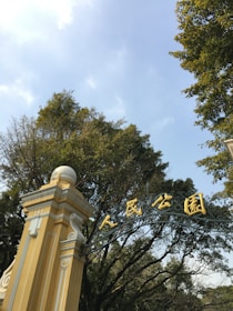 Wide-angle shot of the main entrance gate framed by deep forest green signage and warm sand beige walls.