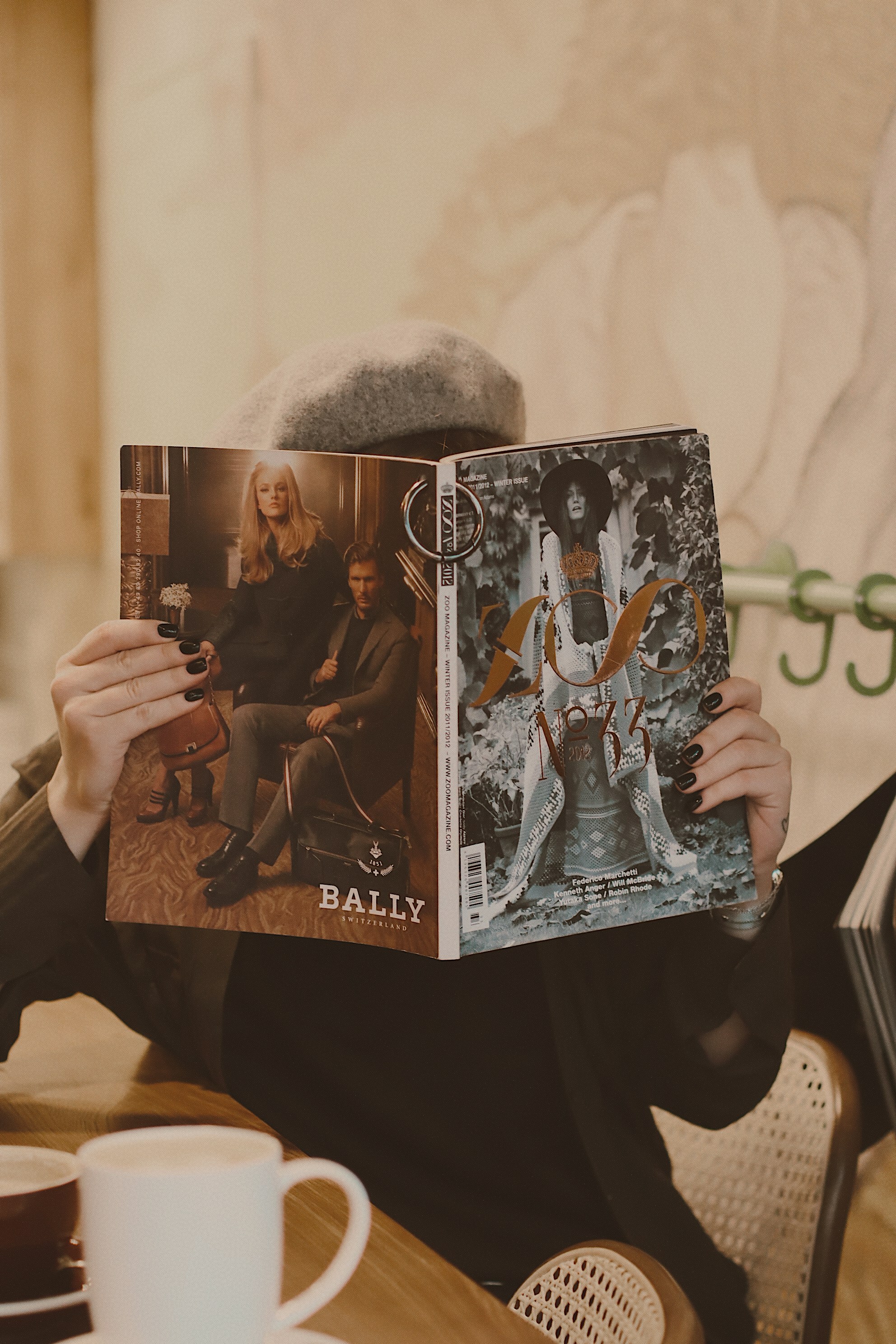 Person in beret holds fashion magazine at wooden table.