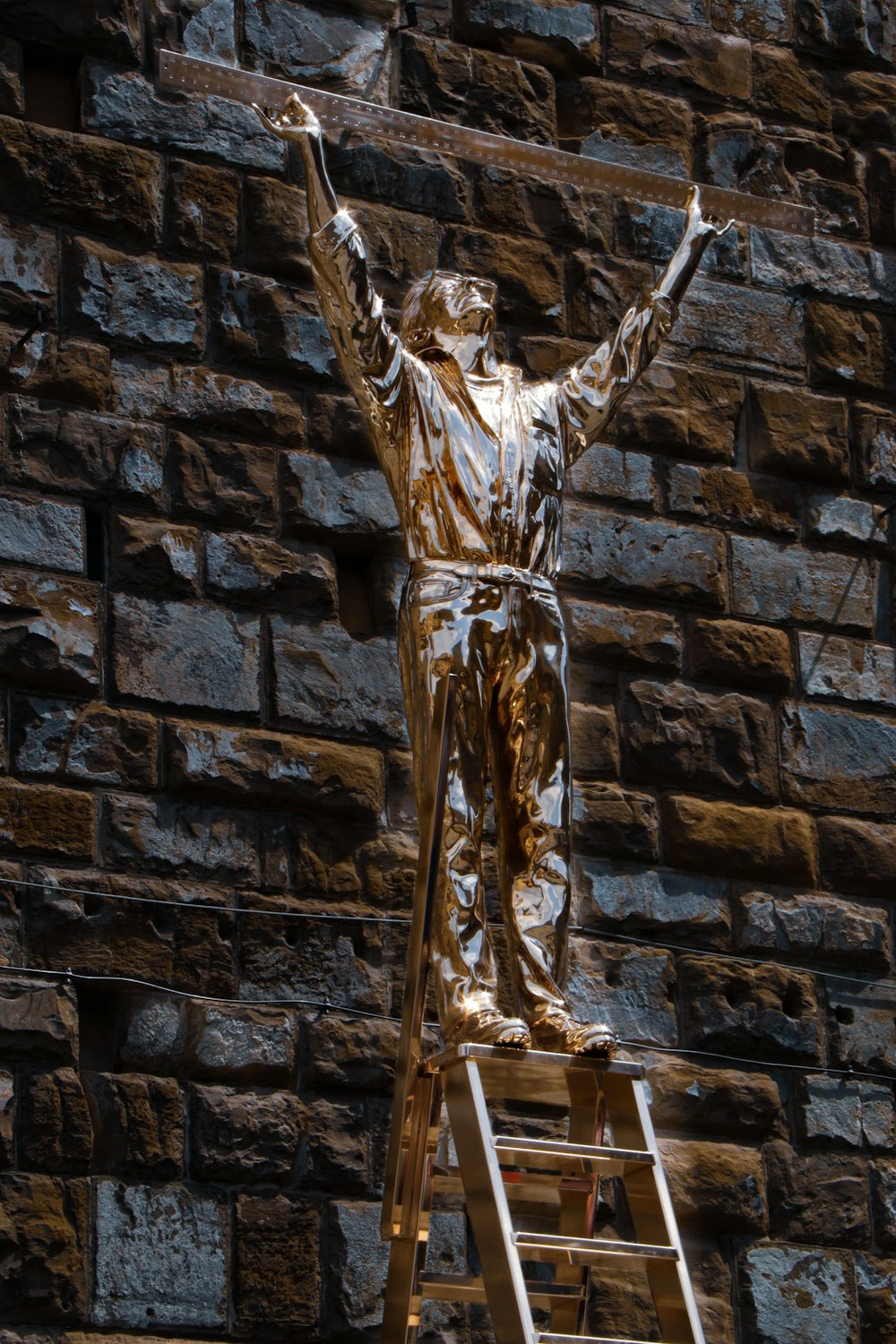 statua d'oro dell'uomo sul muro di mattoni neri