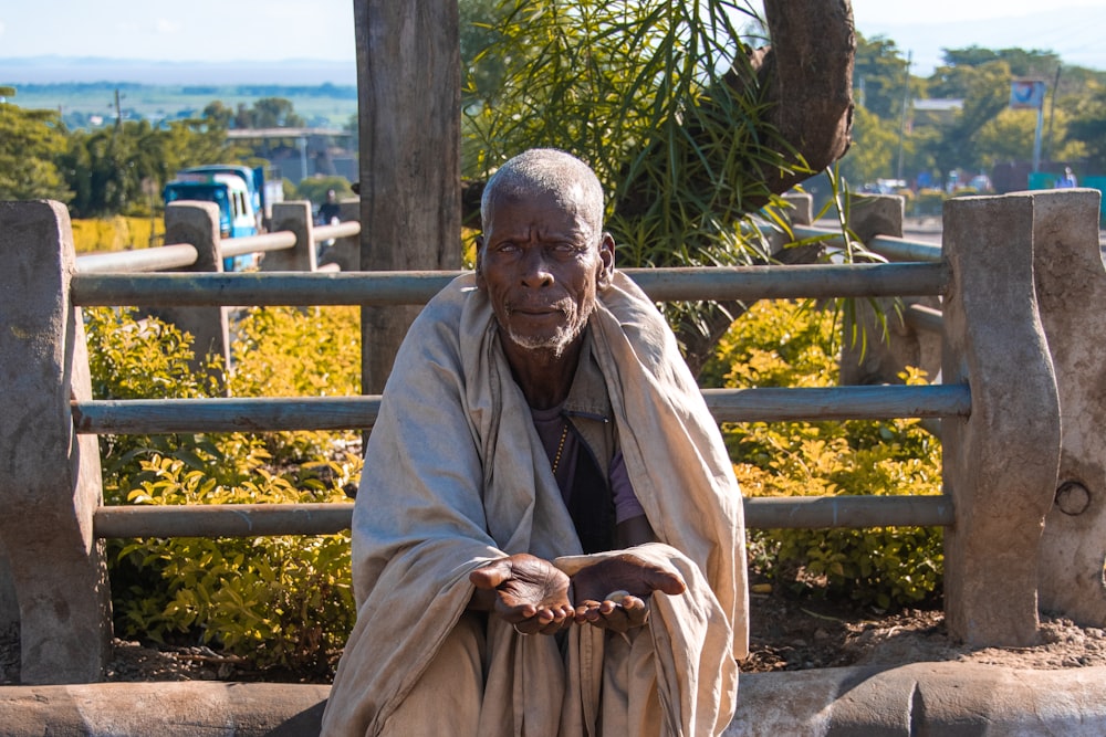 man in brown robe sitting on brown wooden bench during daytime