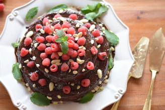 A close-up of a decadent chocolate cake topped with fresh raspberries and mint leaves.