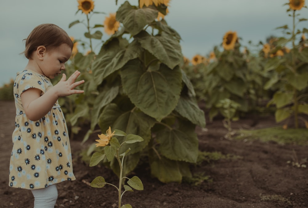 girl in white and blue polka dot dress standing near green leaves during daytime