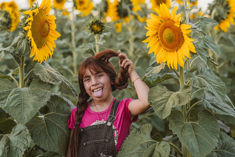 girl in pink and gray tank top standing on sunflower field during daytime