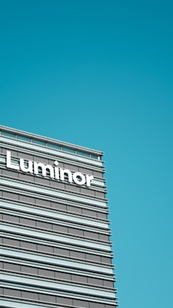A modern office building facade featuring horizontal lines and large windows, with the word 'Luminor' prominently displayed.