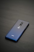 A sleek smartphone with a glossy back, featuring a dual-camera system and a company logo. The phone is placed on a dark, smooth surface, highlighting its elegant design.