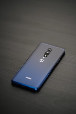 A sleek smartphone with a glossy back, featuring a dual-camera system and a company logo. The phone is placed on a dark, smooth surface, highlighting its elegant design.