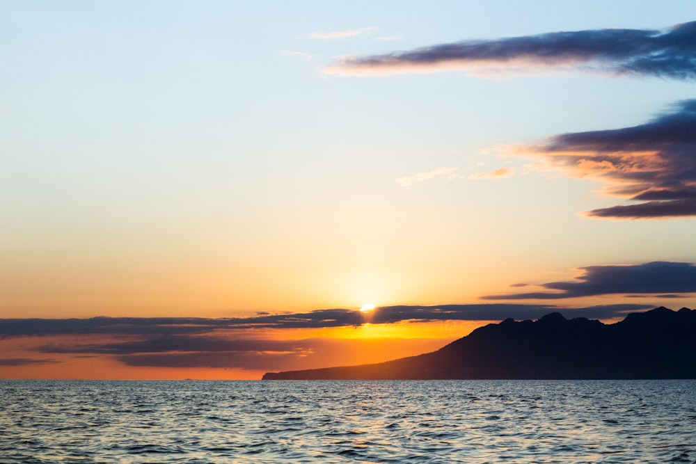 silhouette of mountain near body of water during sunset