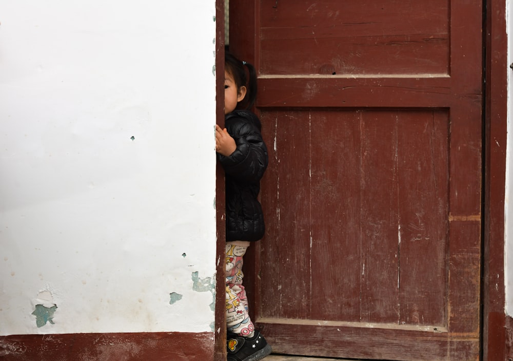 Femme en veste en cuir noir appuyée sur une porte en bois marron