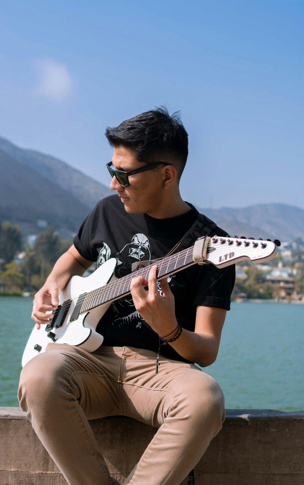 Hombre con camiseta negra de cuello redondo tocando la guitarra eléctrica blanca