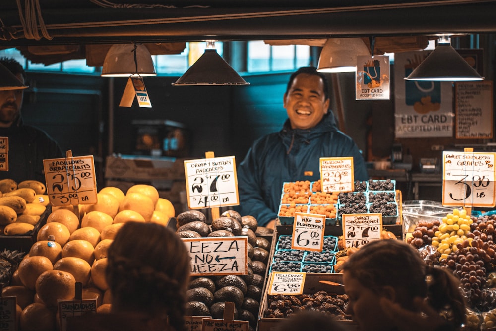 Femme en veste bleue debout devant un stand de fruits