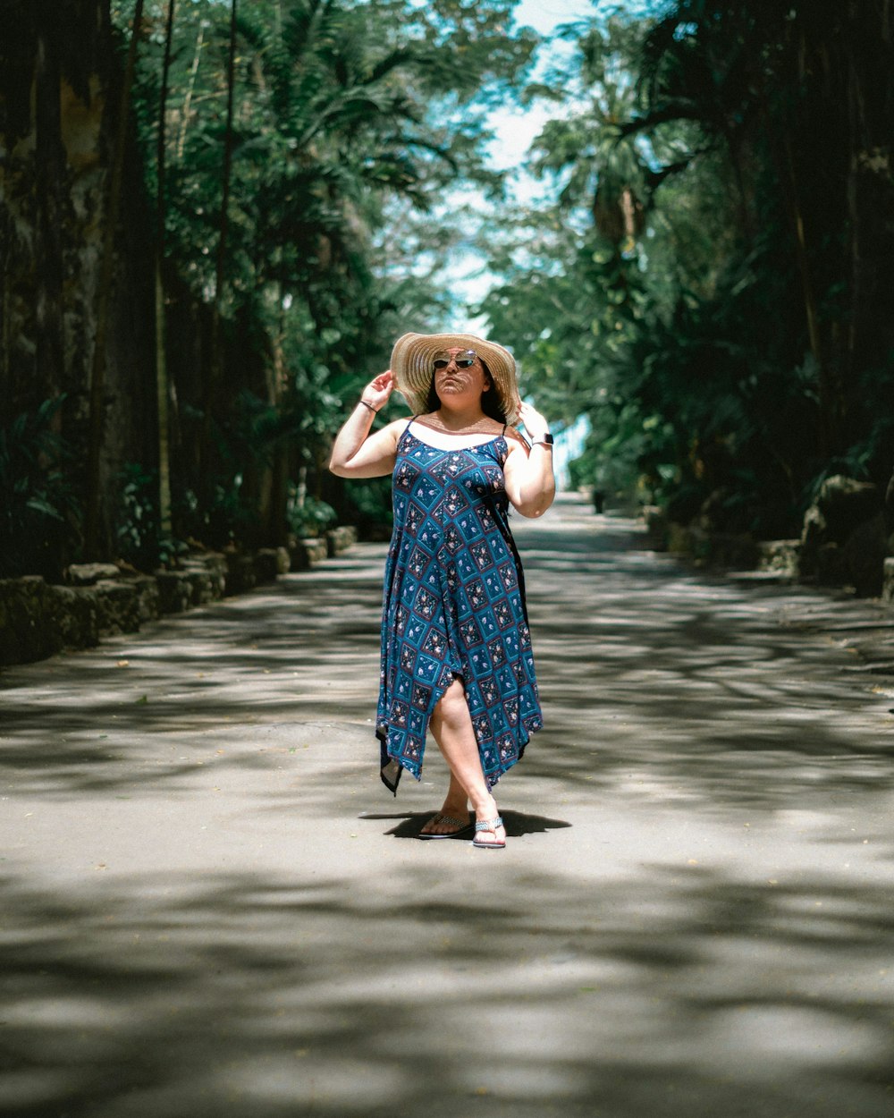 woman in blue and white floral sleeveless dress standing on road during daytime