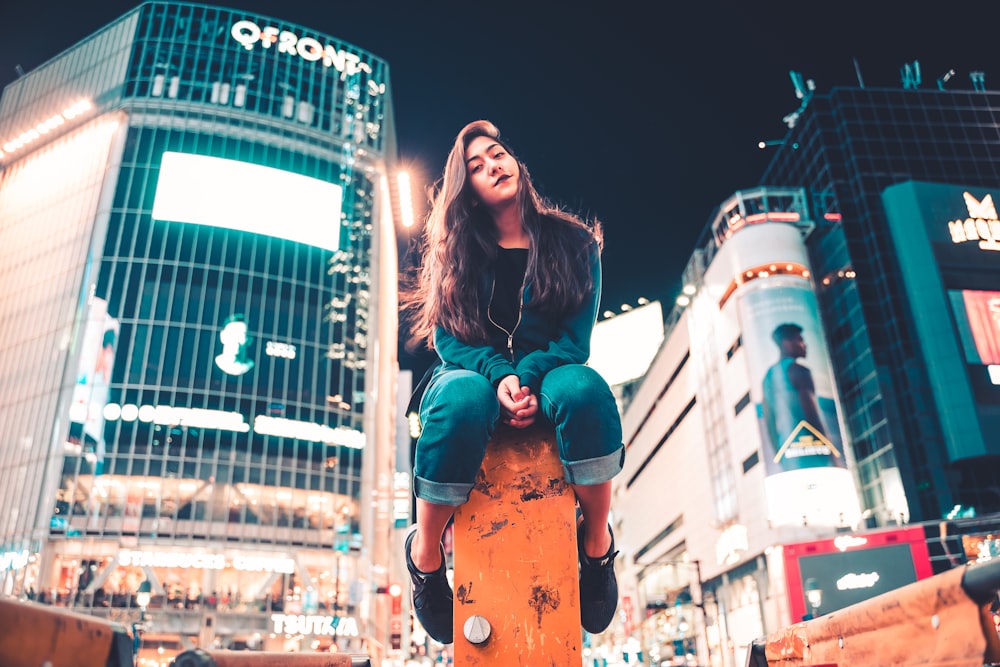 woman in green jacket and blue denim jeans leaning on orange post