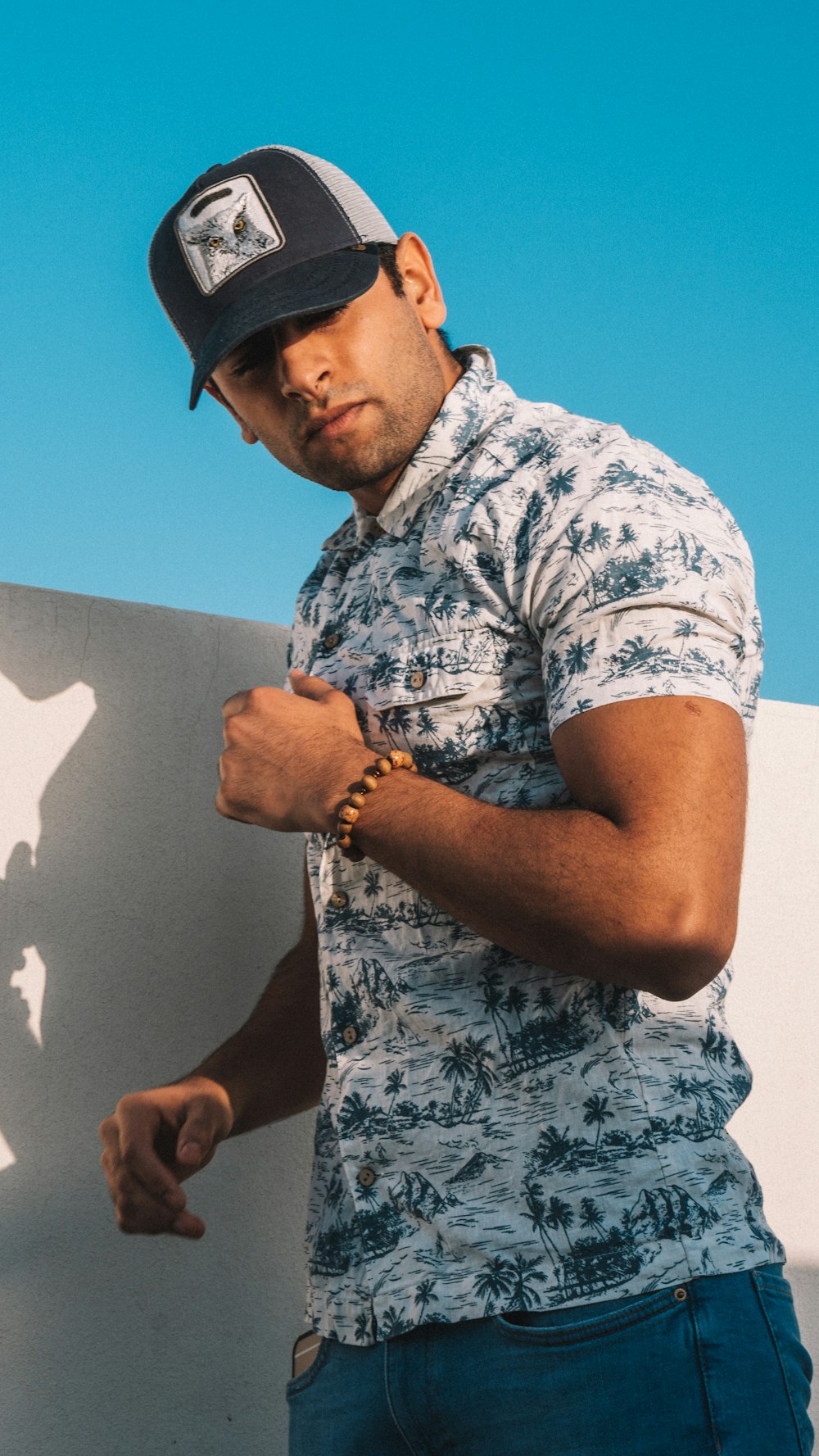 man in grey and white floral button up t-shirt and blue cap holding a black