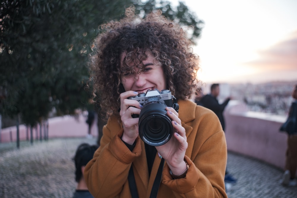 woman in yellow jacket holding black camera