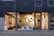 A modern storefront with large glass windows featuring a display of various contemporary lamps and lighting fixtures. The interior is well-lit, showcasing a minimalist and stylish design, with a focus on modern lighting solutions. Visible elements include pendant lamps, floor lamps, and decorative objects arranged neatly. The exterior of the building has a dark-colored facade with vertical paneling.