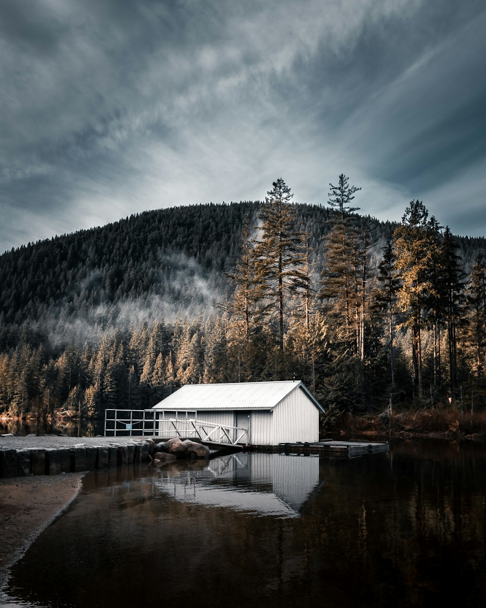 昼間は青空の下、木々に囲まれた湖畔の白い木造家屋