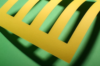 A bright yellow piece of paper with five evenly spaced rectangular cutouts is placed against a green background, casting shadows that create a play of light and shade.