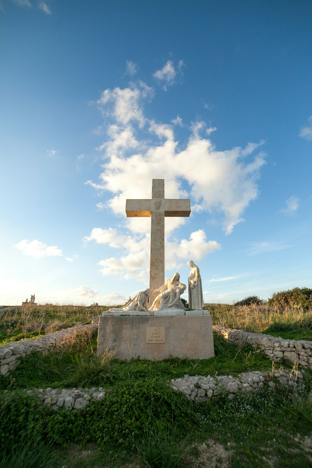 graues Betonkreuz auf grünem Gras unter weißen Wolken tagsüber