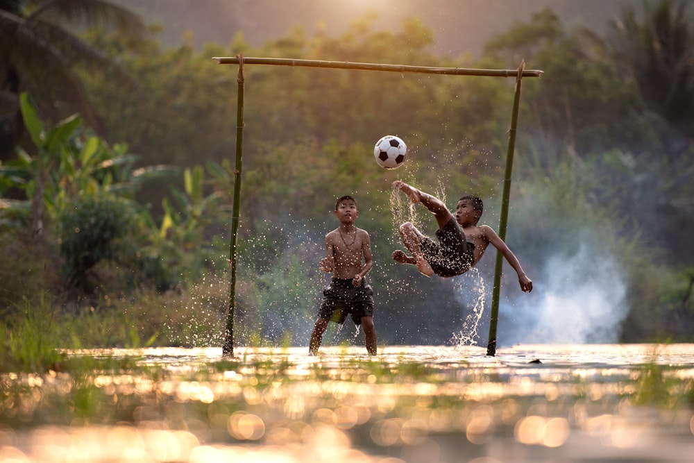 2 boys playing soccer on water during daytime
