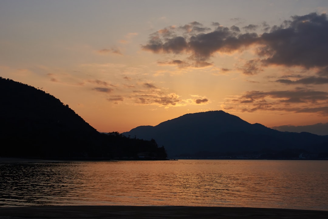 silhouette of mountain near body of water during sunset