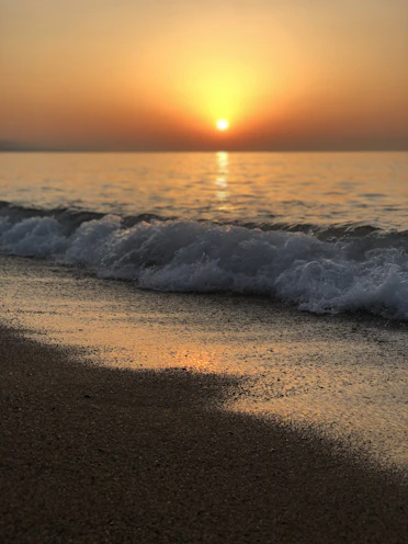 ocean waves crashing on shore during sunset