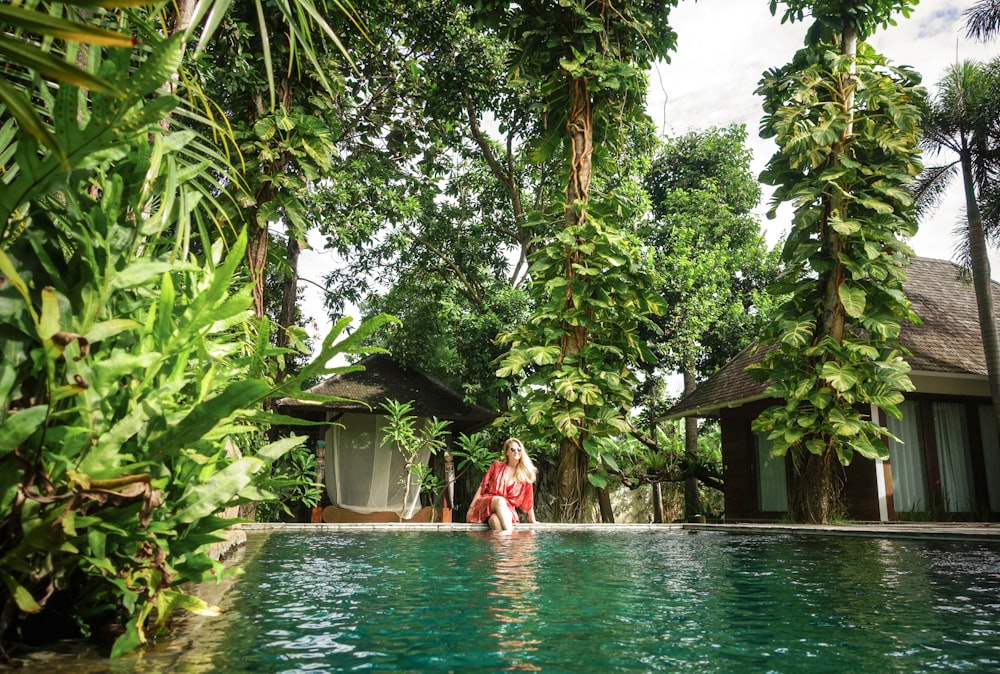 woman in red dress standing on green water near green trees during daytime