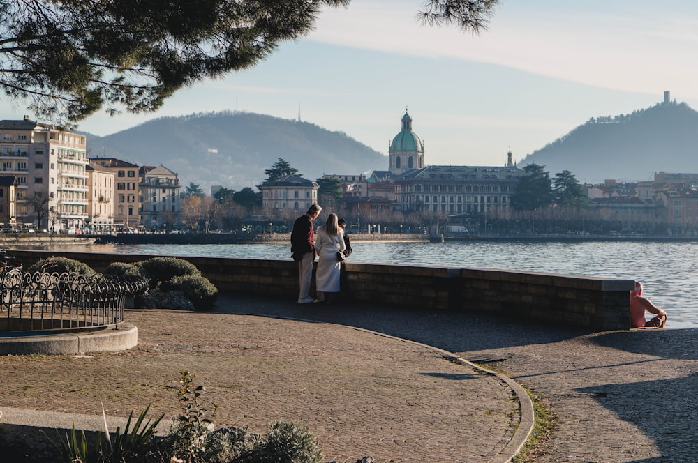 couple standing on concrete bridge near body of water during daytime