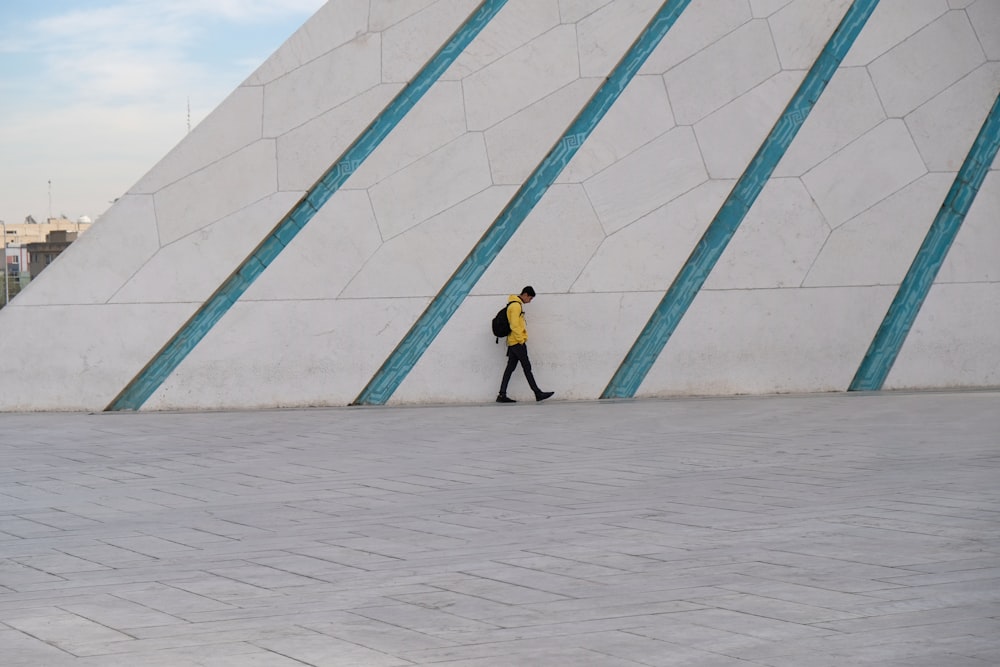 woman in yellow jacket and black pants standing beside blue wall during daytime