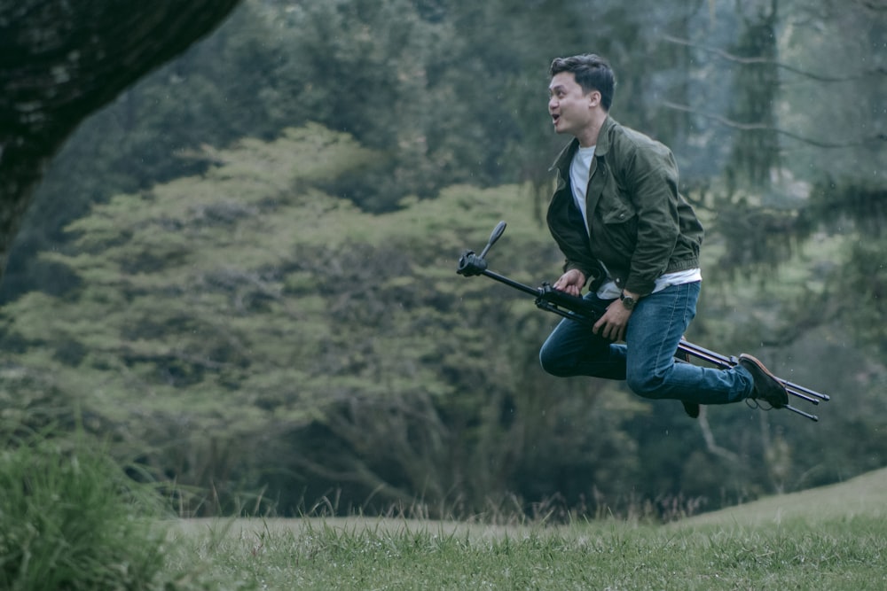 man in green jacket and blue denim jeans holding black camera on green grass field during