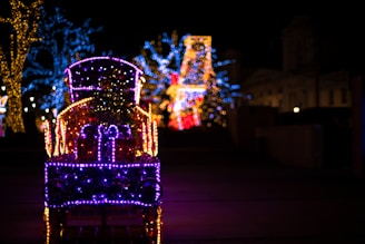 A festive train decorated for the holidays, surrounded by snow-covered trees and twinkling lights.