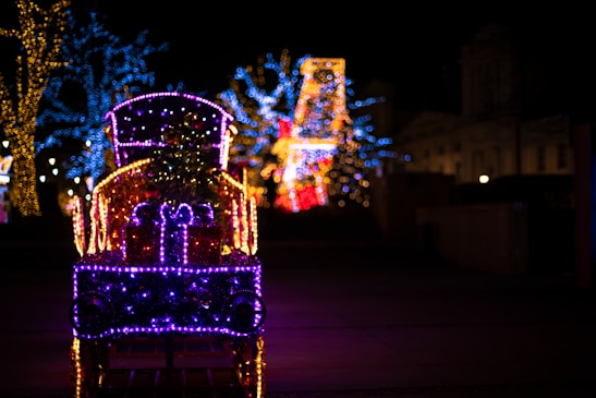 A festive train decorated for the holidays, surrounded by snow-covered trees and twinkling lights.