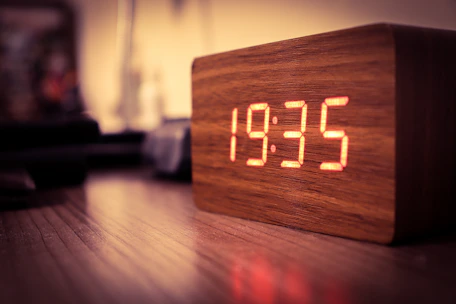 A sleek digital clock glowing softly on a wooden bedside table.