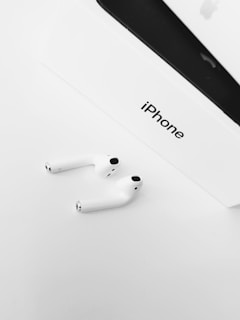 Close-up of an Apple iPhone with a glossy finish, resting beside stylish wireless earbuds on a minimalist white surface.