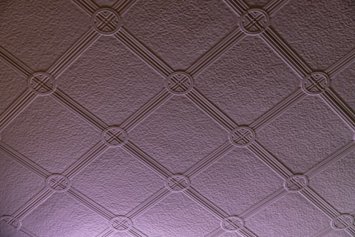 A textured ceiling pattern featuring a grid of interlocking circles and diagonal lines. The surface has a subtle texture, and the pattern is consistent across the entire surface.