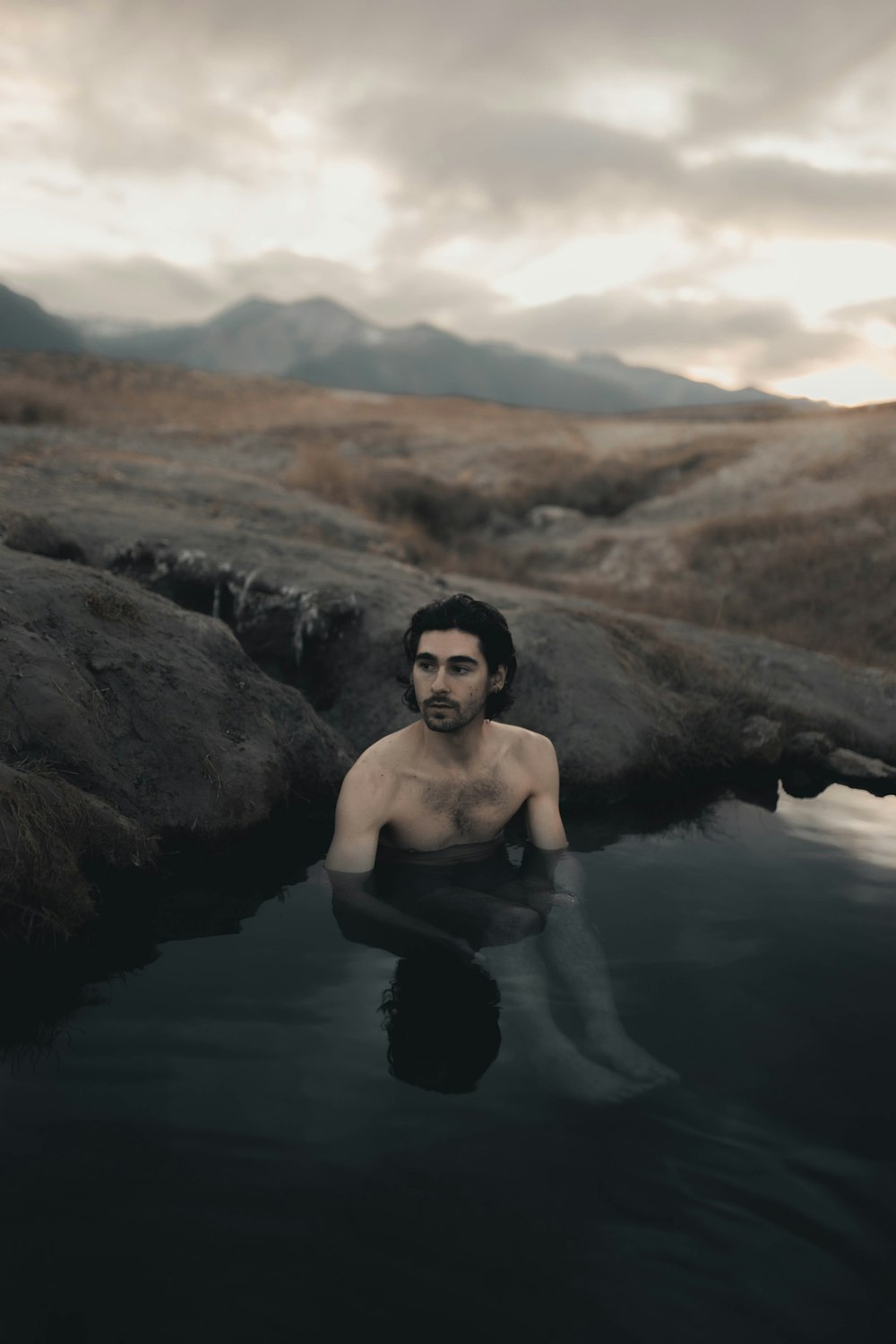 topless woman in black pants sitting on rock in river during daytime